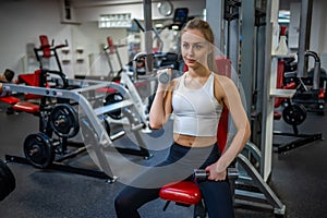 Young woman holds dumbbells in her hands and works out in the gym performing an exercise