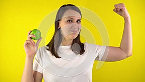 A young woman holds a green apple in her hand. A girl in a white T-shirt smiles and shows strength in her hand. The