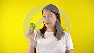 A young woman holds a green apple in her hand. A girl in a white T-shirt smiles and winks at the camera. The concept of