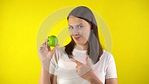 A young woman holds a green apple in her hand. A girl in a white T-shirt twists an apple, smiles and shows a super sign