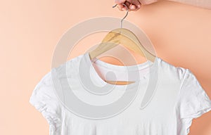 Young woman holds in hand wooden hanger with white cotton T-shirts hanging on it on pink background. Casual unisex clothes