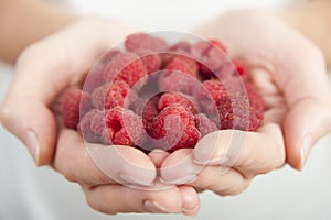 Young woman holds handful of fresh raspberries