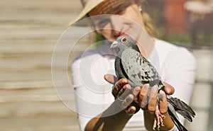 A young woman holds in the hands of a mail pigeon.  She is looking forward to his return from a long journey