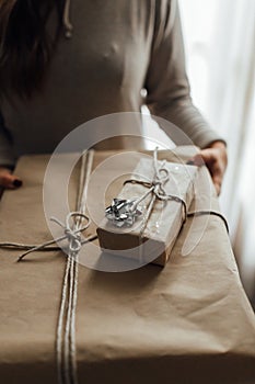 Young woman holds in hands stacked Christmas gift boxes in craft paper with juniper. Christmas presents concept