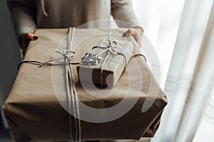 Young woman holds in hands stacked Christmas gift boxes in craft paper with juniper. Christmas presents concept