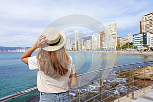 Young woman holds hat on promenade in front of the skyline from Benidorm Downtown, Spain