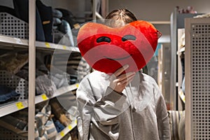 A young woman holds a heart-shaped pillow in her hands in a store.