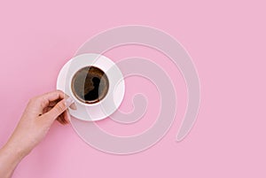 A young woman holds in her hand a white cup of coffee on a pink background. Place for text. Top view