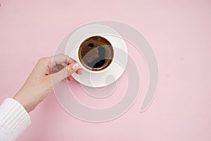 A young woman holds in her hand a white cup of coffee on a pink background. Place for text. Top view