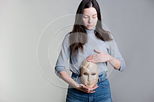 A young woman holds a mask with her face at the level of her stomach.