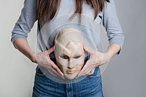 A young woman holds a mask with her face at the level of her stomach.