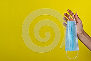 A young woman holds a medical face mask in her hand. Protective mask on a yellow background in the girl`s hand.