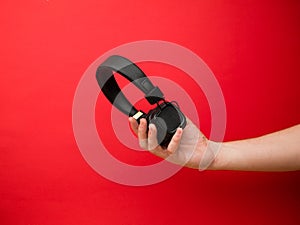 A young woman holds a pair of black wireless headphones in her hand. Hand of a girl with headphones on a red background