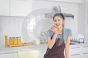 A young woman holds a red apple in the kitchen with a cheerful face