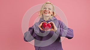 Young woman holds red paper heart on her chest. Symbol romantic love. Woman in purple hoodie with red heart in her hands