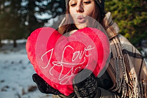 Young woman holds a red pillow heart in winter forest
