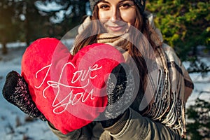 Young woman holds a red pillow heart in winter forest