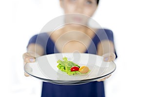 Young woman holds small portion salad on studio