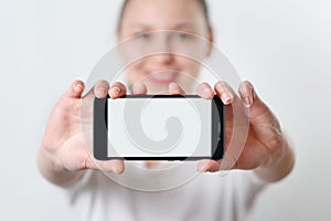 A young woman holds the smartphone horizontally with a white screen with a place for copyspace. on light background