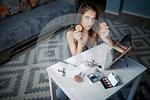 Young woman holds sponges before mirror.