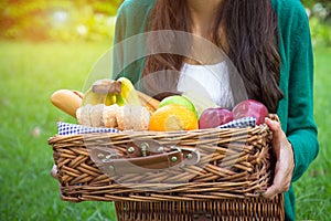 Young woman holds straw basket with healthy food, bananas, apple, orange, corn, whole wheat bread vegetables and fruits