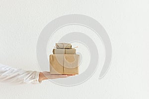 Young woman holds on stretched hand palm stacked Christmas gift boxes in craft paper. Holiday corporate presents delivery service