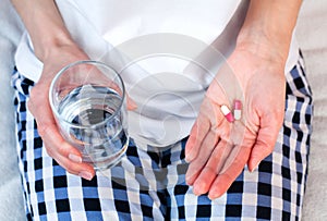 Young woman holds two pills and glass of water in hands. Taking vitamins, supplements, antibiotic, painkiller medication.