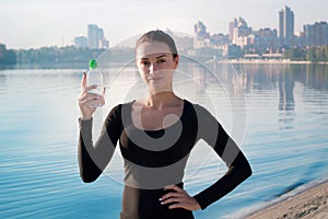 Young woman holds water bottle at river and city backround