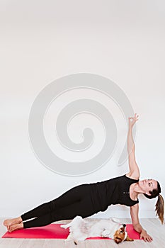 Young woman at home doing yoga on a mat. cute small dog besides. healthy lifestyle concept