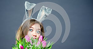 Young woman at home easter celbration concept in a bunny ears holding decorative eggs on sticks and buquet of tulips