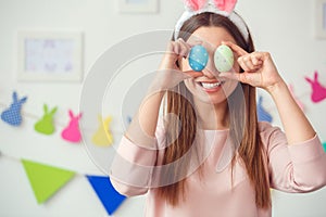 Young woman at home easter celbration concept in a bunny ears holding eggs covering eyes