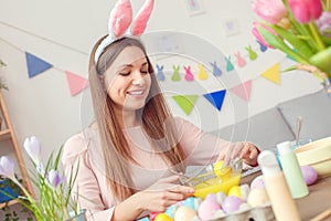 Young woman at home easter celbration concept in a bunny ears sitting coloring egg using food color