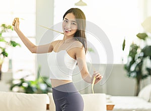 A young woman at home, holding a measuring ruler while dancing, is very satisfied with her posture, very happy to lose weight