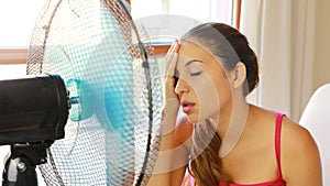 Young woman at home in hot summer day in front of the working fan suffering from summer heat