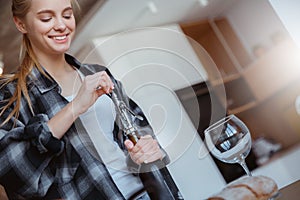 Young woman at home in the kitchen opening wine photo