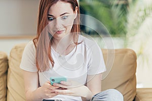 Young woman at home receiving positive emotions winning and good news while reading phone while sitting on sofa