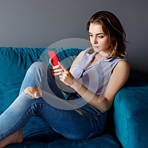 Young woman at home relaxing on the couch, using smartphone.