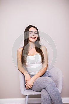 Young woman at home sitting on modern chair in front of window relaxing in her living room, stretching with closed eyes.