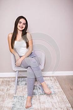 Young woman at home sitting on modern chair in front of window relaxing in her living room, stretching with closed eyes.