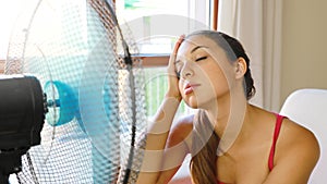 Young woman at home with working fan in hot summer day suffering heat