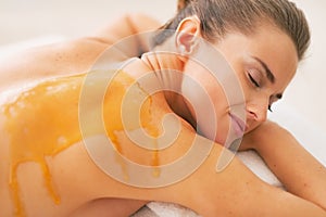 Young woman with honey on back laying on massage table