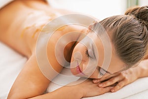 Young woman with honey on back laying on massage table