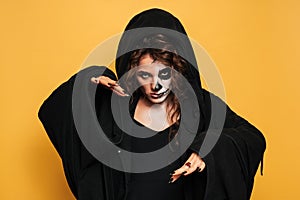 A young woman in a hood with scary makeup. on a yellow isolated background. Concert costume party. Banner.