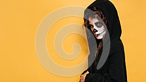 A young woman in a hood with scary makeup. on a yellow isolated background. Concert costume party. A place for your text