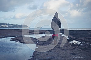 Young woman in hooded coat walking on beach