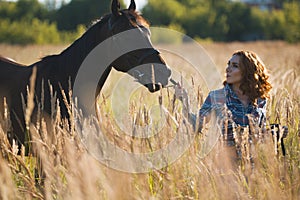 Young woman and horse in the meadow at summer evening