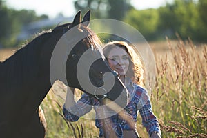 Young woman and horse in the meadow at summer evening