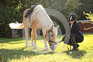 Young woman in horse riding suit and her beautiful pet outdoors on sunny day