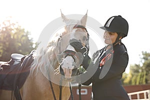 Young woman in horse riding suit and her beautiful pet outdoors on sunny day