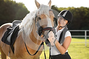 Young woman in horse riding suit and her beautiful pet outdoors on sunny day